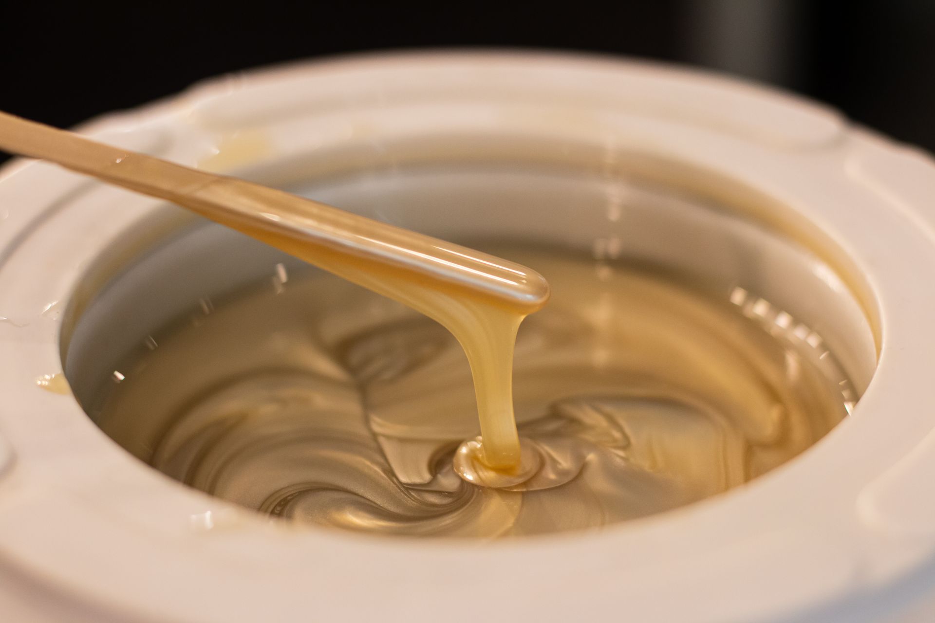 A bowl of wax with a wooden spoon in it.