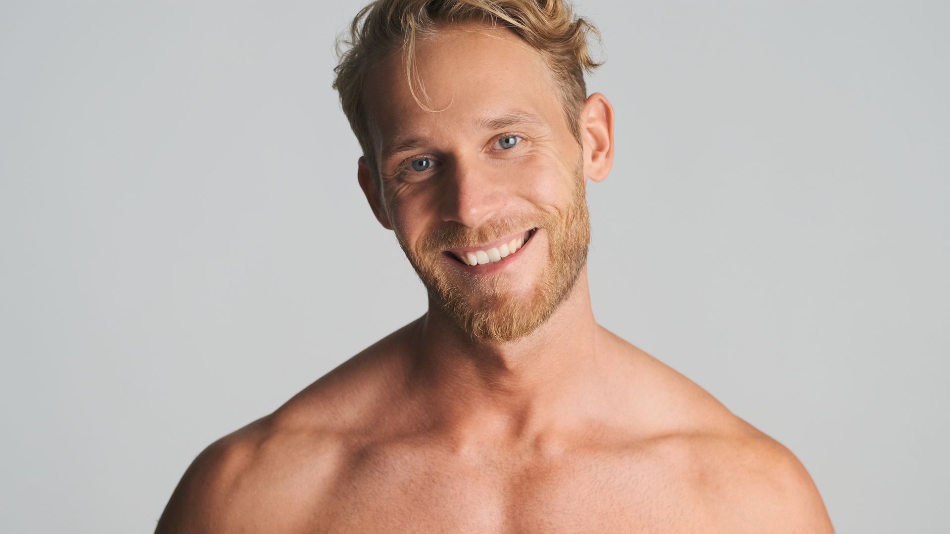 A shirtless man with a beard is smiling for the camera.