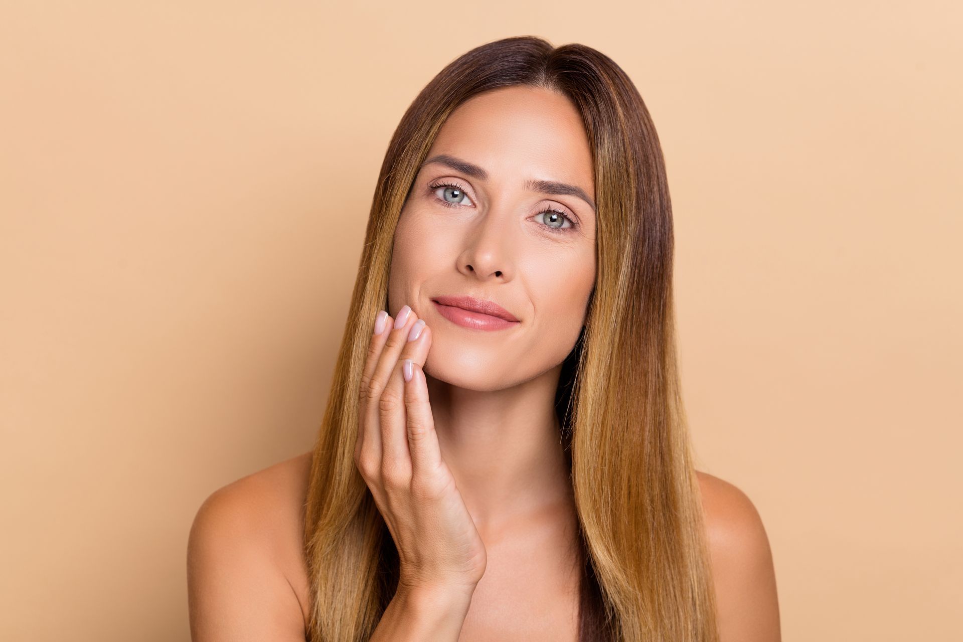 A woman is touching her face with her hands and smiling.