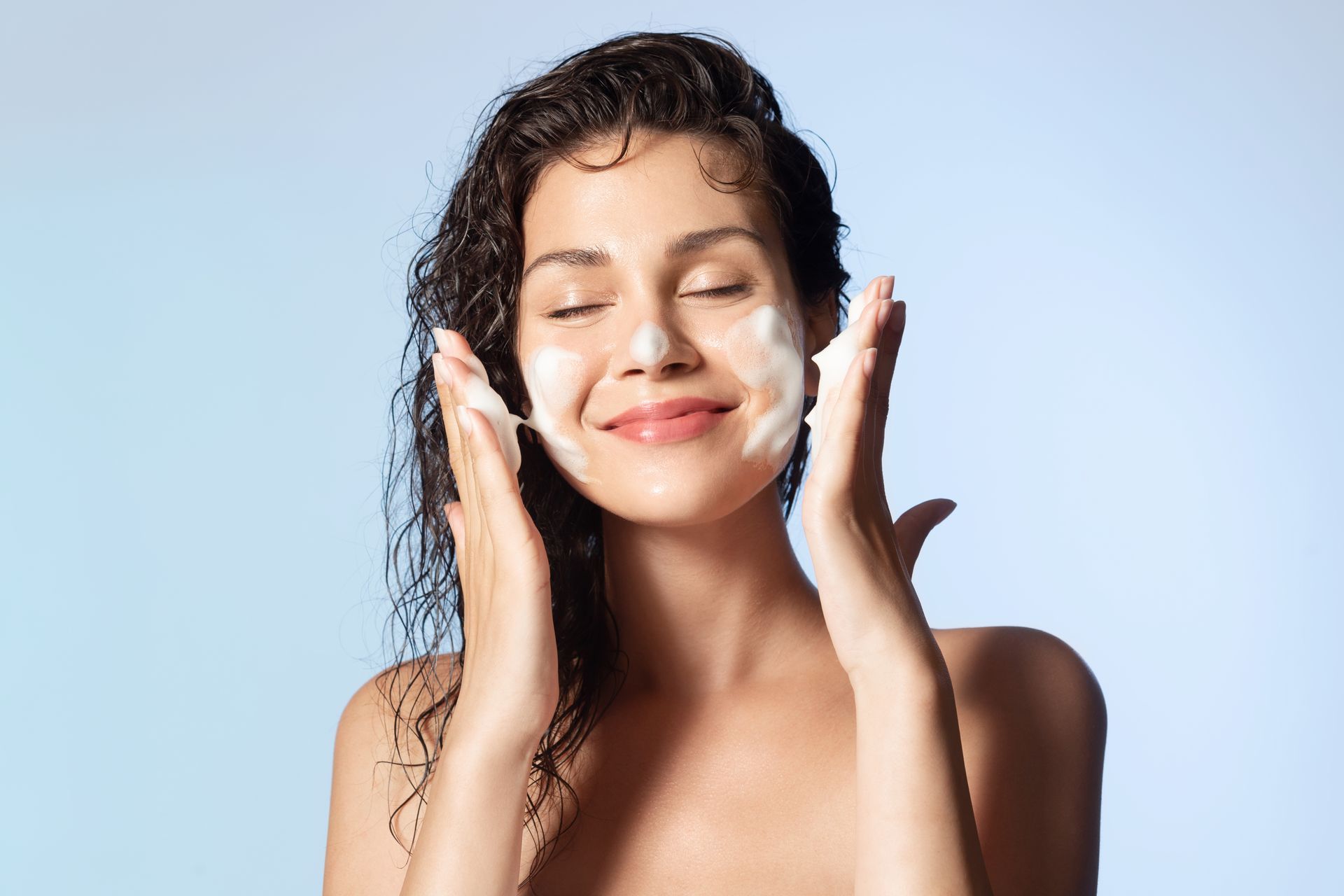 A woman is washing her face with soap and smiling.