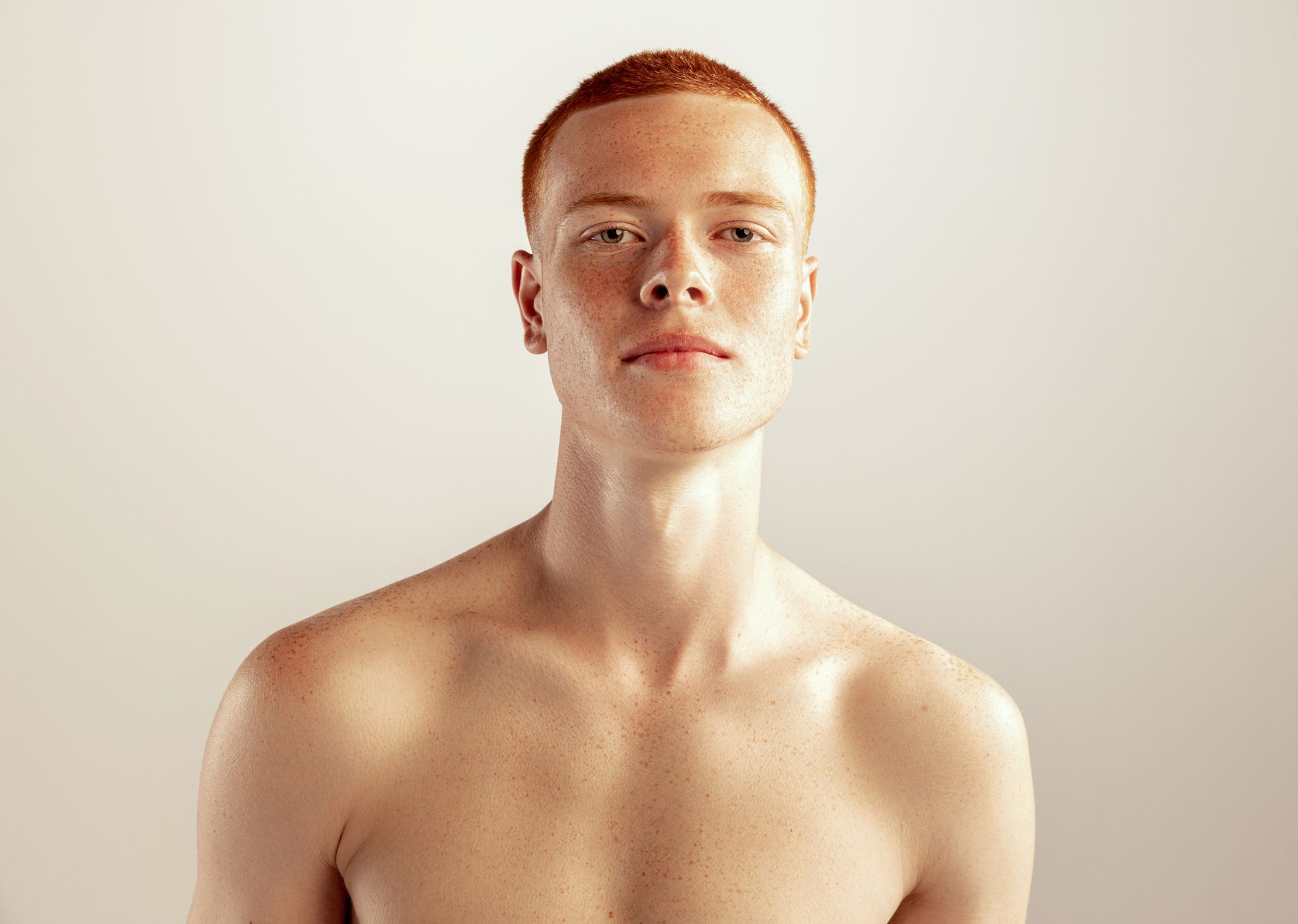 A shirtless young man with red hair is looking at the camera.