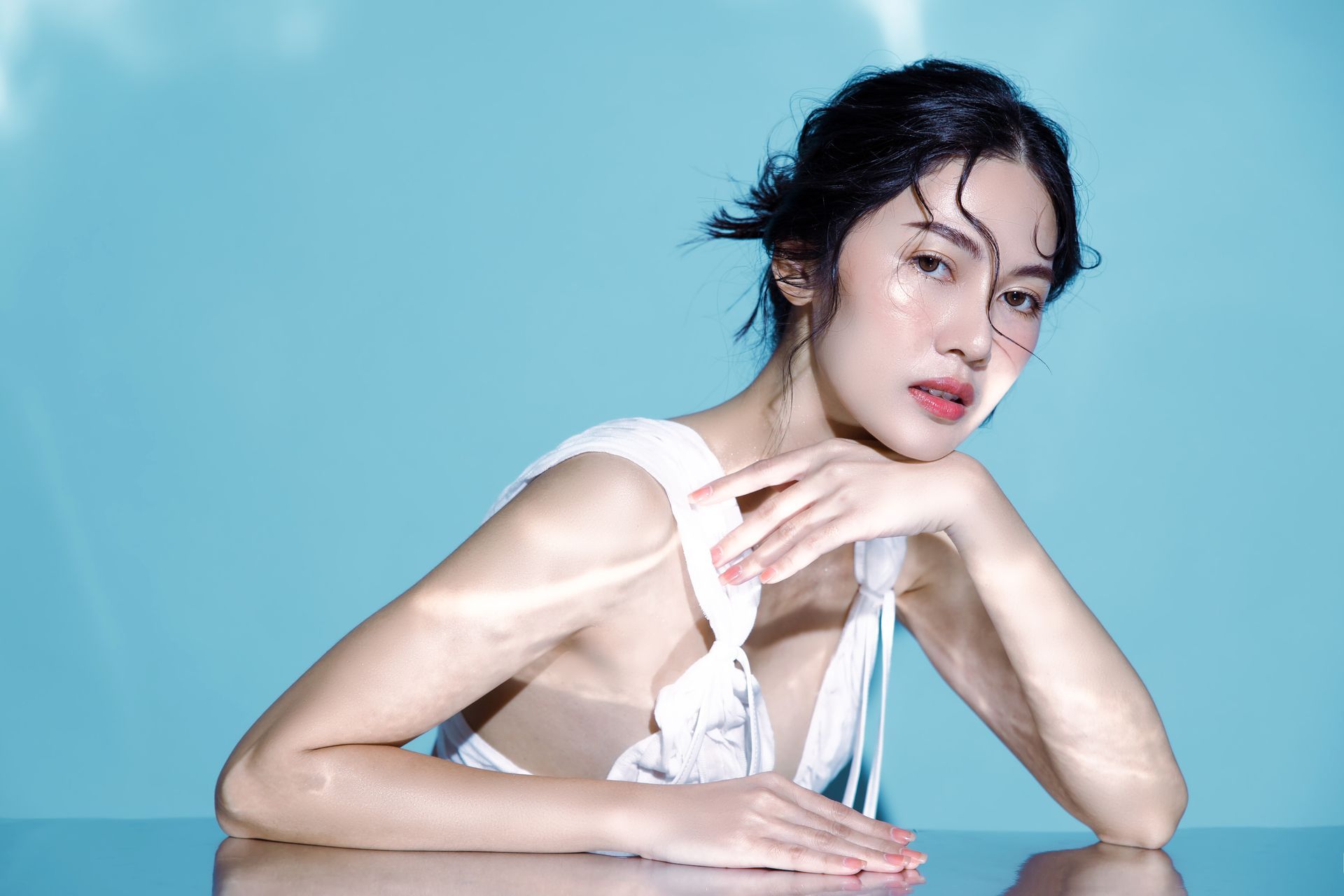 A woman in a white dress is sitting at a table with her hands on her face.