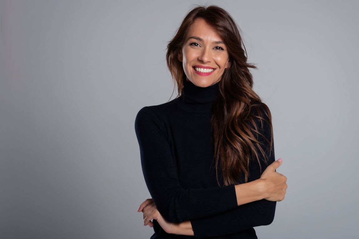 A woman in a black turtleneck sweater is smiling with her arms crossed.