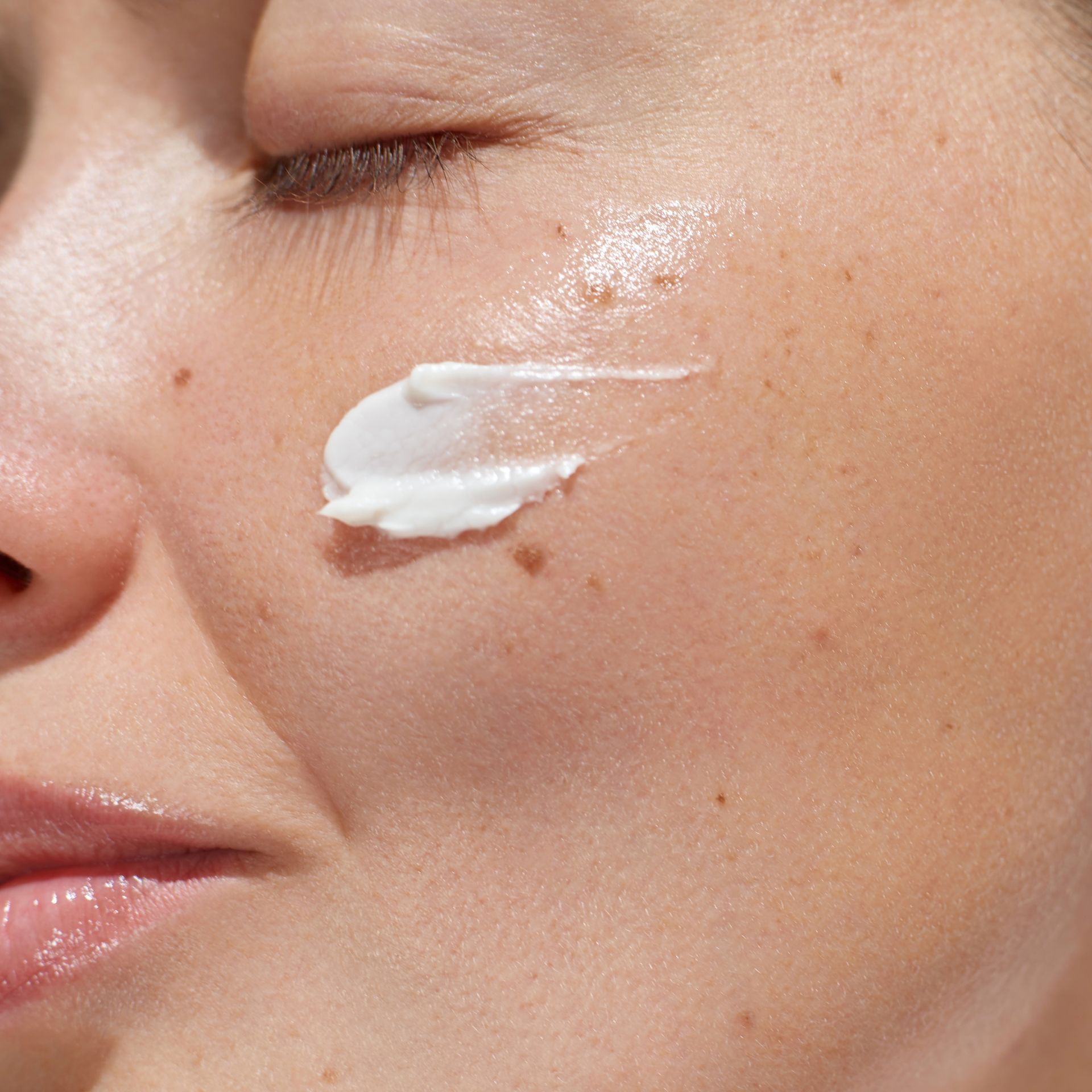 A close up of a woman applying cream to her face.