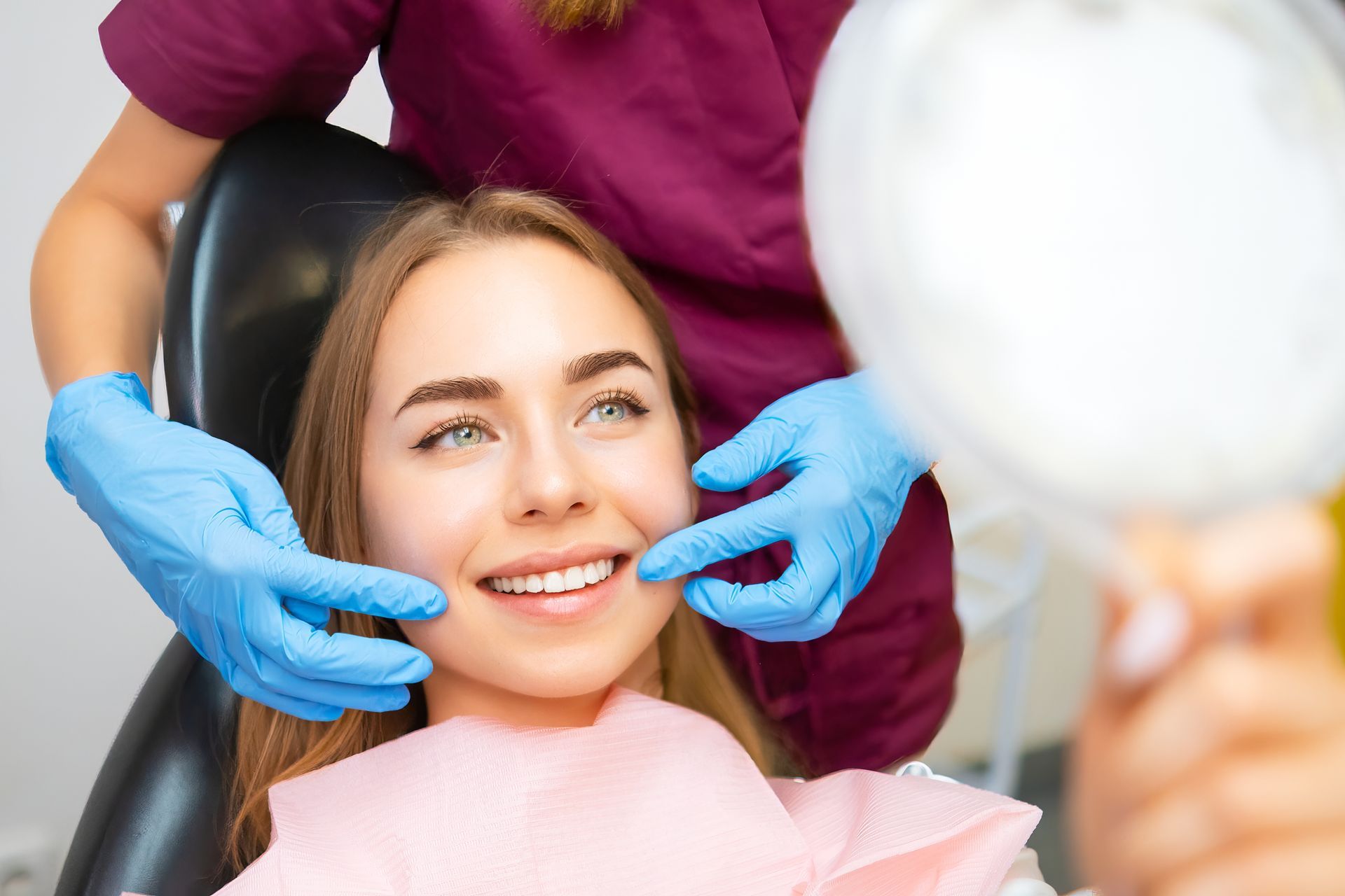 A woman is sitting in a dental chair while a dentist examines her teeth.