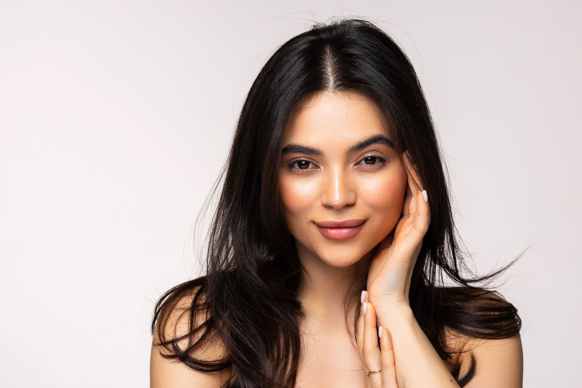 A woman with long hair is touching her face with her hand and smiling.