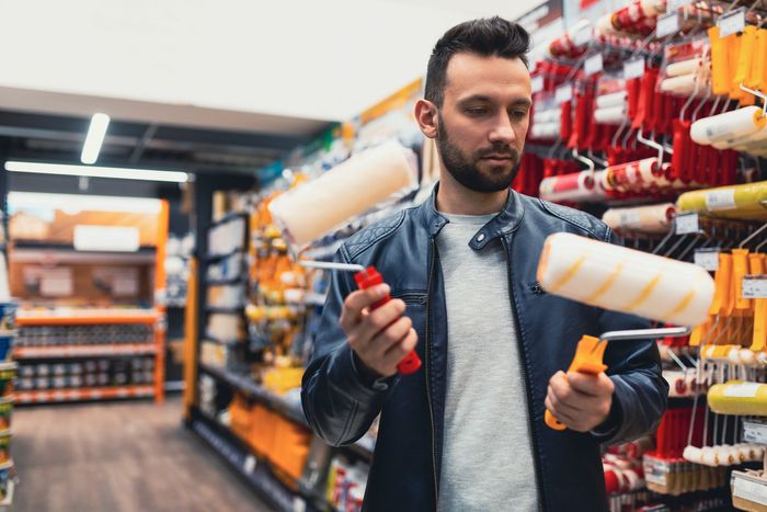 A man is holding a paint roller in a hardware store.