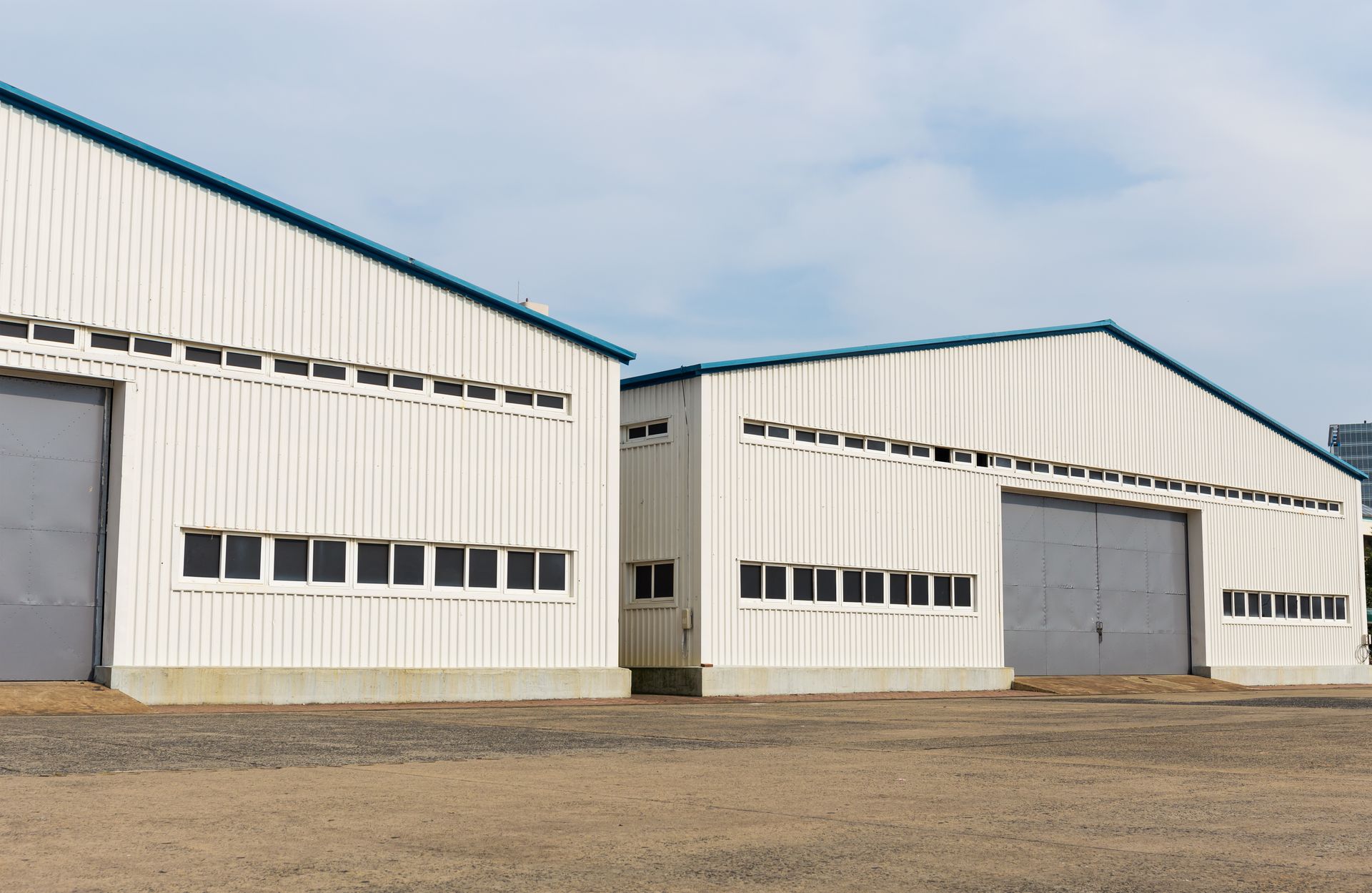 A row of white warehouses with gray doors in a dirt field.