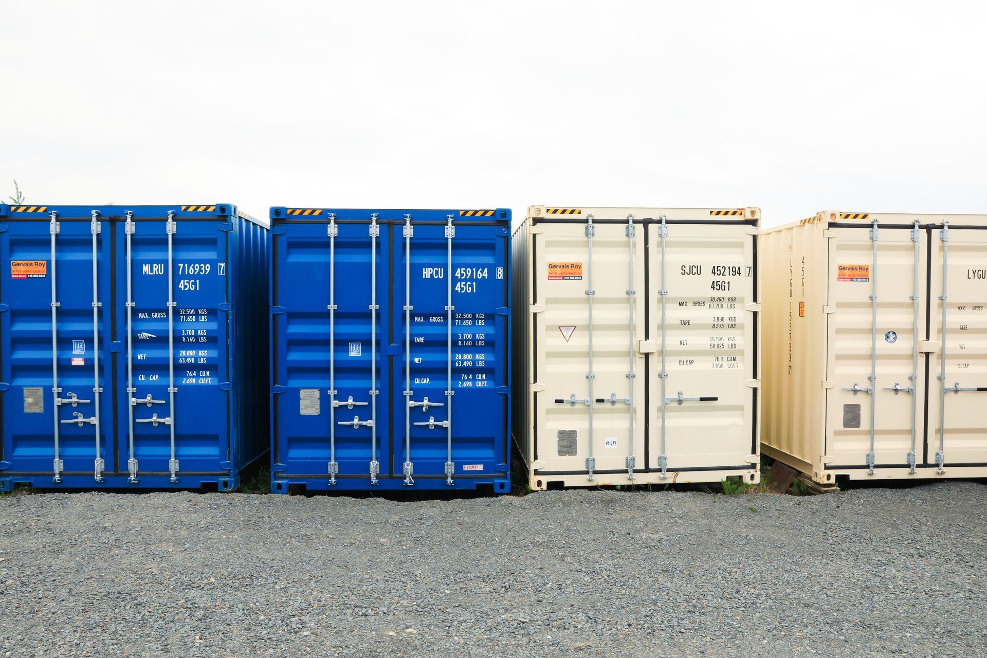 Une rangée de conteneurs d'expédition est alignée sur un terrain en gravier.