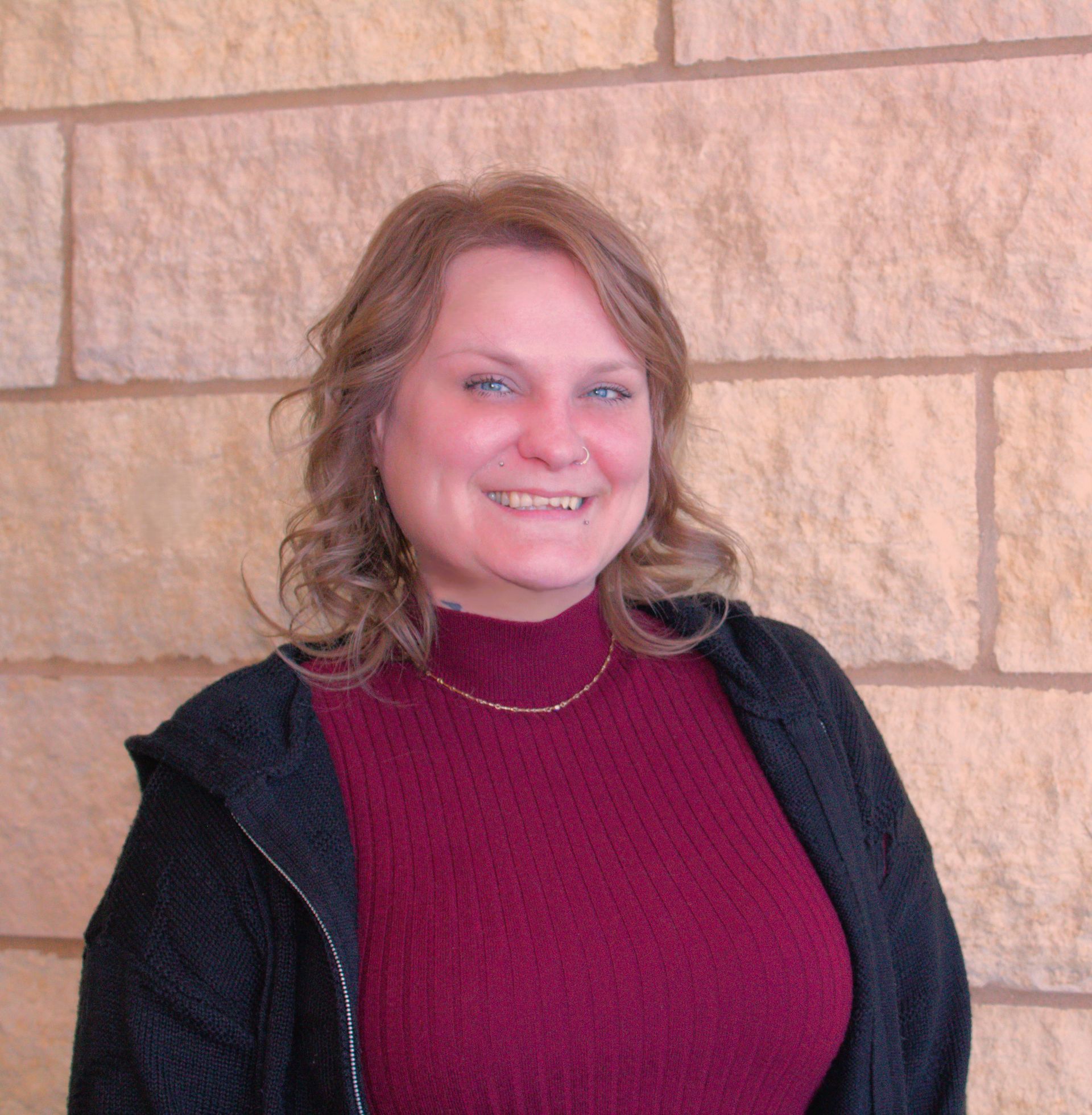 An addiction education counselor in a pink sweater is smiling for the camera.