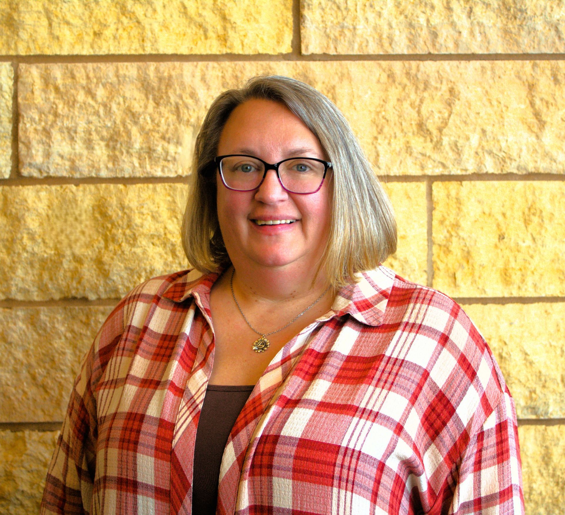 An addiction education counselor wearing glasses and a floral shirt is smiling for the camera.