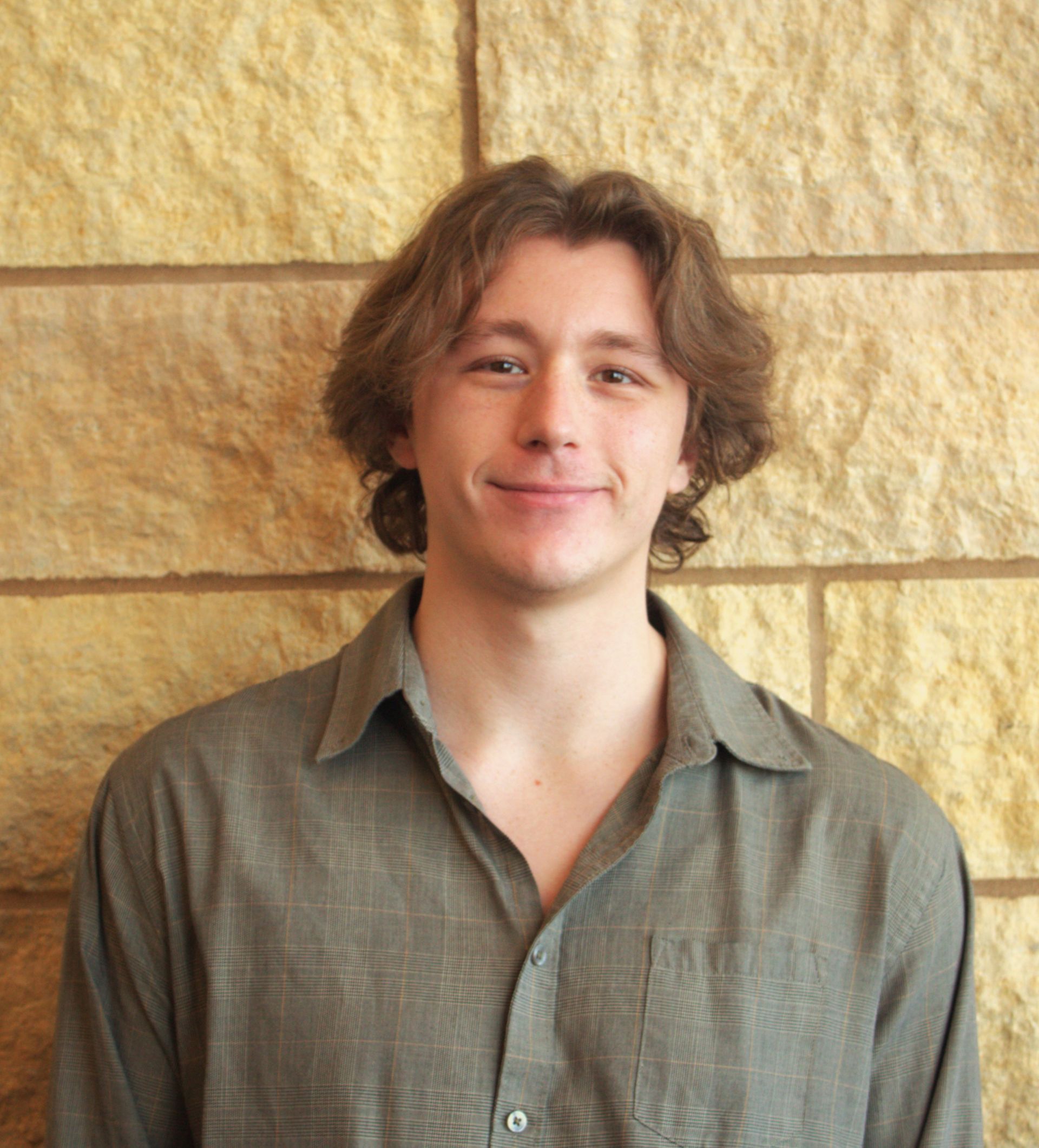 An addiction education counselor wearing a black sweater and a silver chain is standing in front of a white wall.