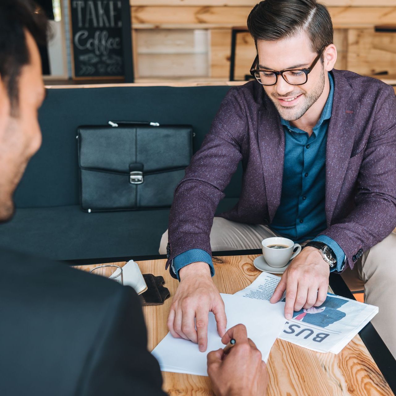 A man in a purple jacket is sitting at a table talking to another man
