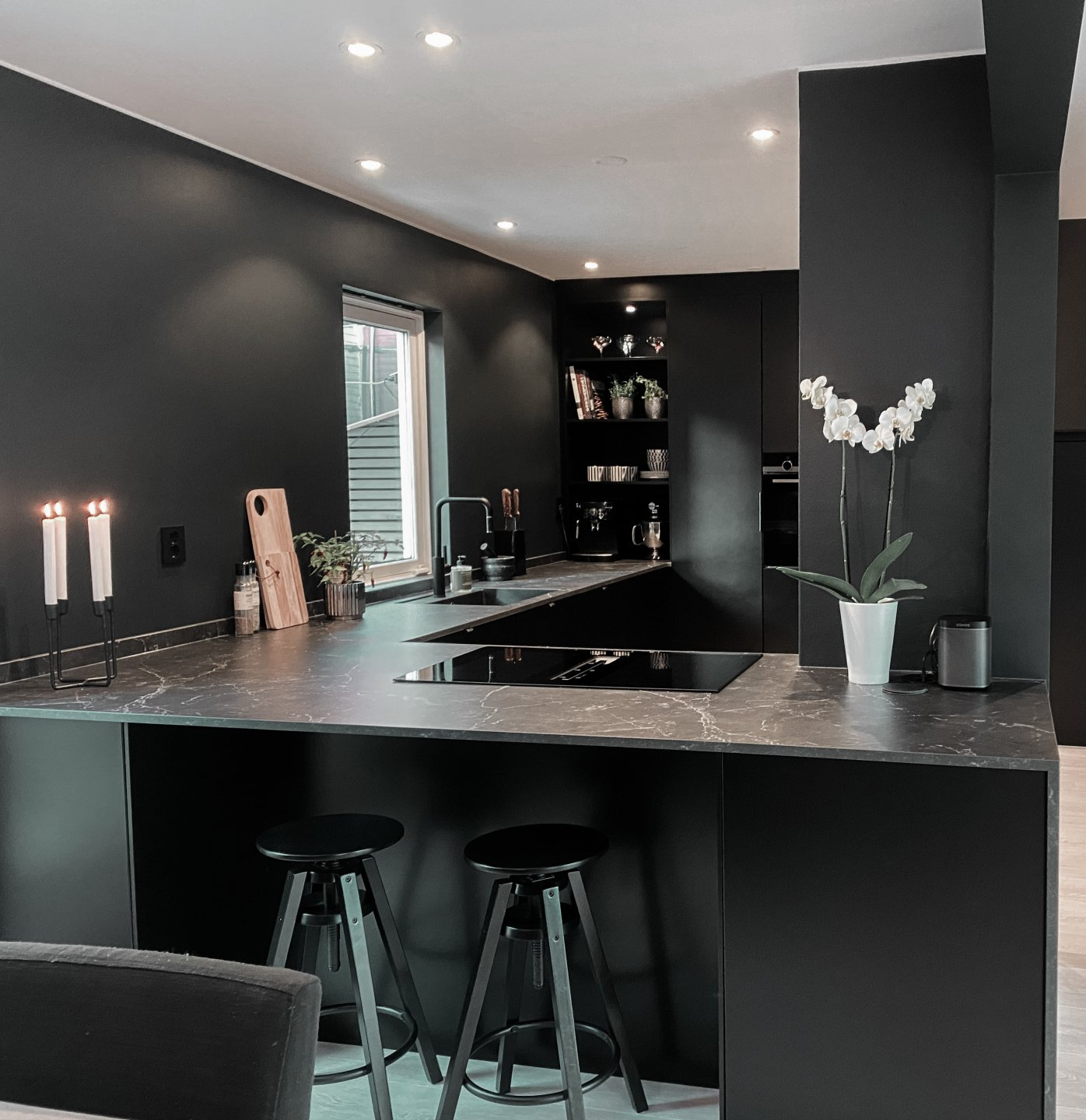 Dark modern kitchen with black cabinets, countertops, and stools. White orchid and candles provide contrast.