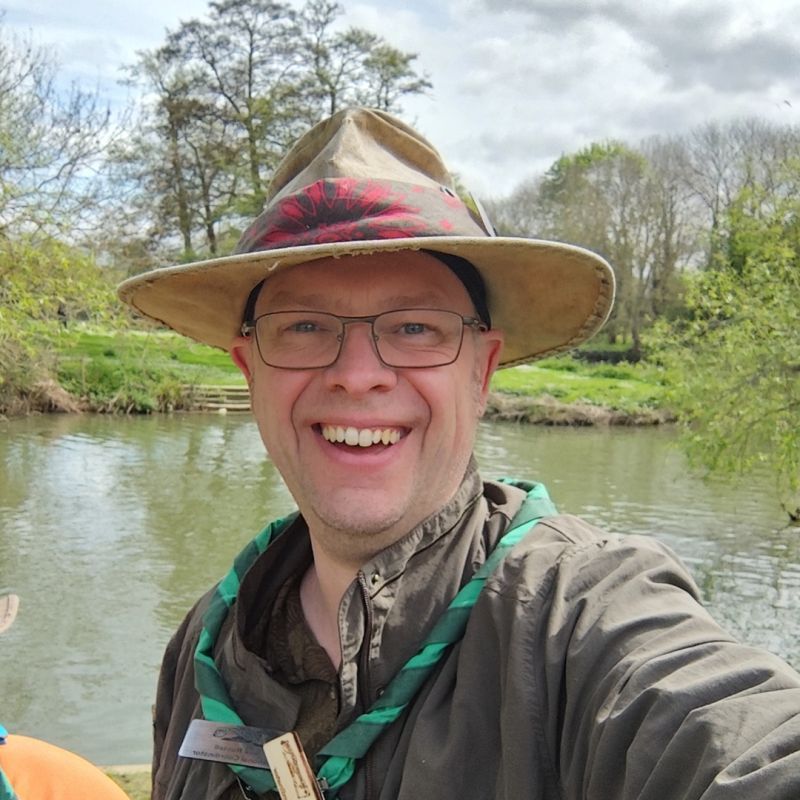 National Manager Lee Russell wearing a hat, Bushscout necker, smiling beside a river.