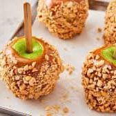 A close up of a tray of caramel apples with nuts on a table.