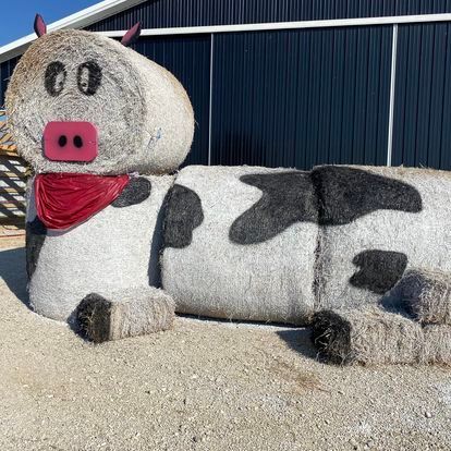 A statue of a cow made out of hay with a red scarf around its neck.