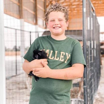 A young boy in a green shirt is holding a black rabbit.