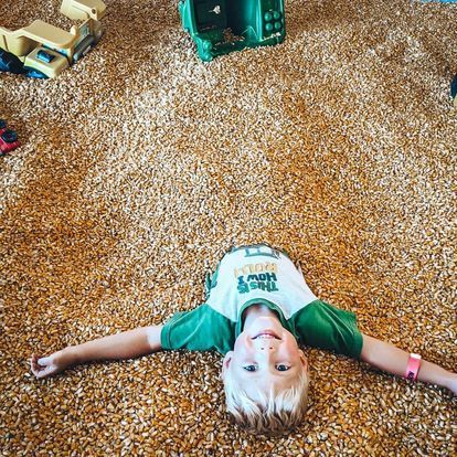 A young boy is laying on his back on a pile of corn.