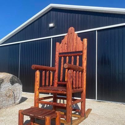 A large wooden rocking chair is sitting in front of a barn