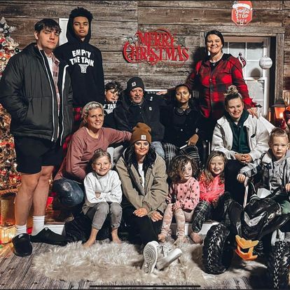 A large family is posing for a christmas photo in front of a christmas tree.