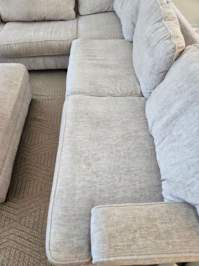 Beige sectional sofa with light gray cushions in a carpeted living room.