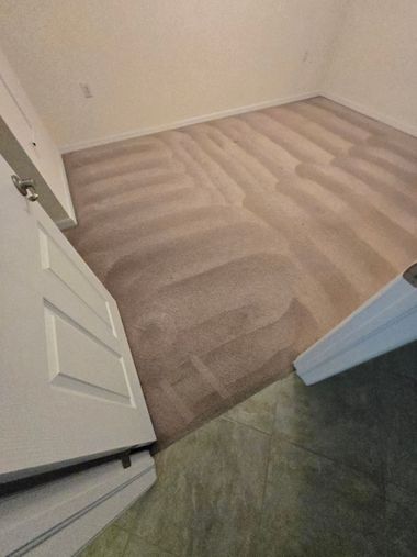 Open door view into an empty beige bedroom with carpet and white walls.