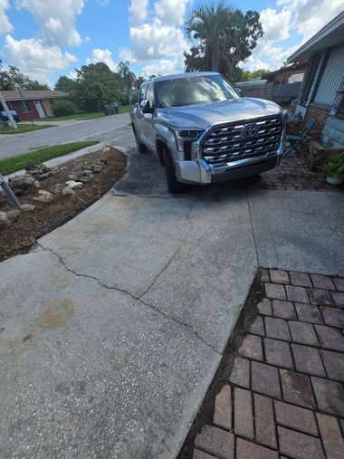 Silver SUV parked on a narrow concrete driveway beside a house and lawn.