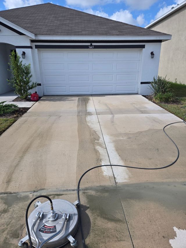 Pressure washer on a driveway in front of a white garage, cleaning the concrete.