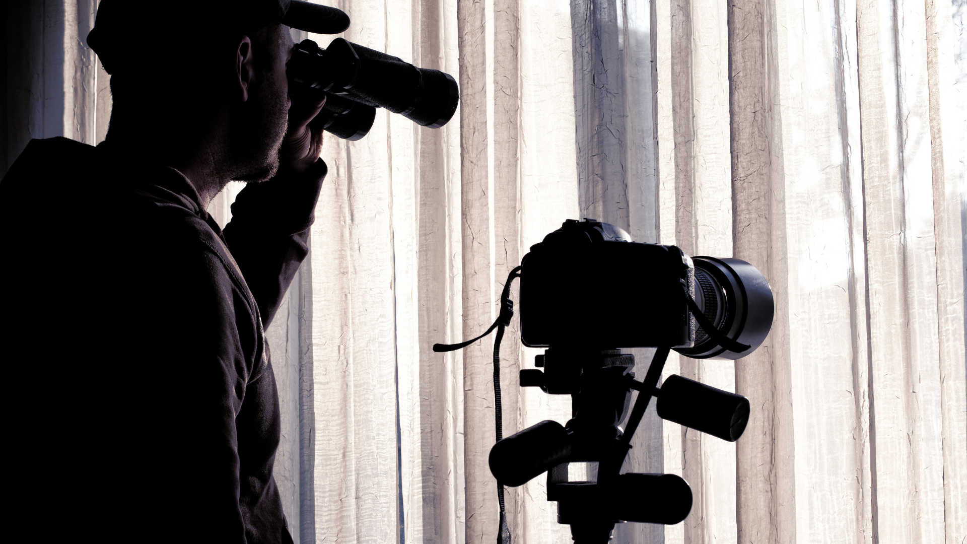 Silhouette of a person with a camera, taking a picture near a window with a camera on a tripod.