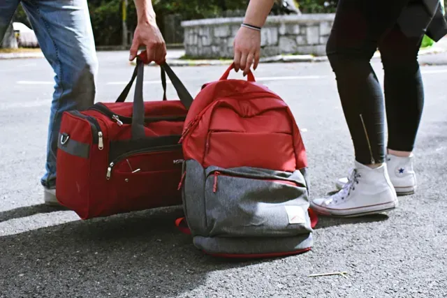 Duas pessoas carregando uma mochila vermelha e uma mochila no asfalto.