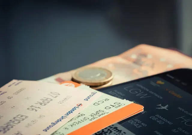 Passagens aéreas, dinheiro, moedas e tela de celular exibindo detalhes do voo, tudo disposto em uma superfície.