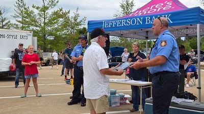 Two uniformed officials present an award to a person under a Jefferson Bank tent during an outdoor community event.