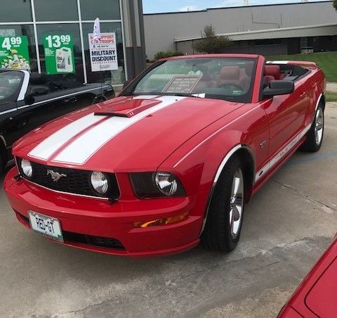 A red Ford Mustang convertible with white racing stripes parked outside a building.