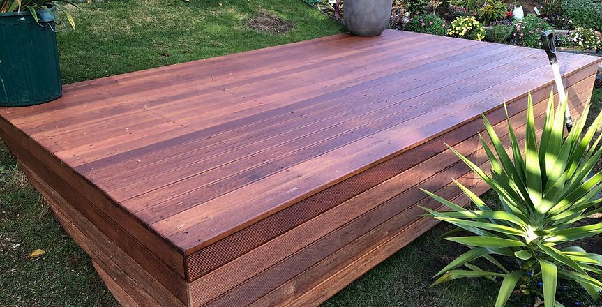 A wooden deck is sitting on top of a lush green lawn next to a potted plant.