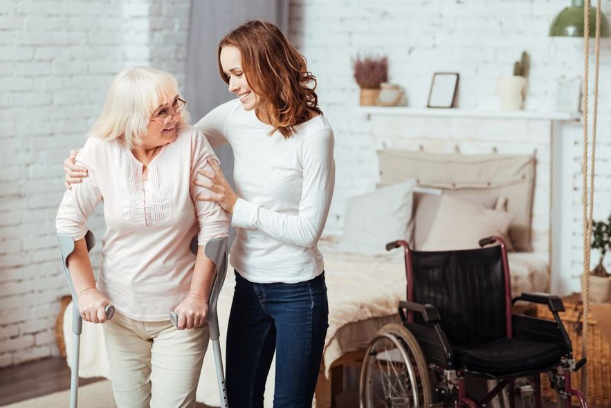 A woman is holding the hand of an elderly man while sitting in a chair.