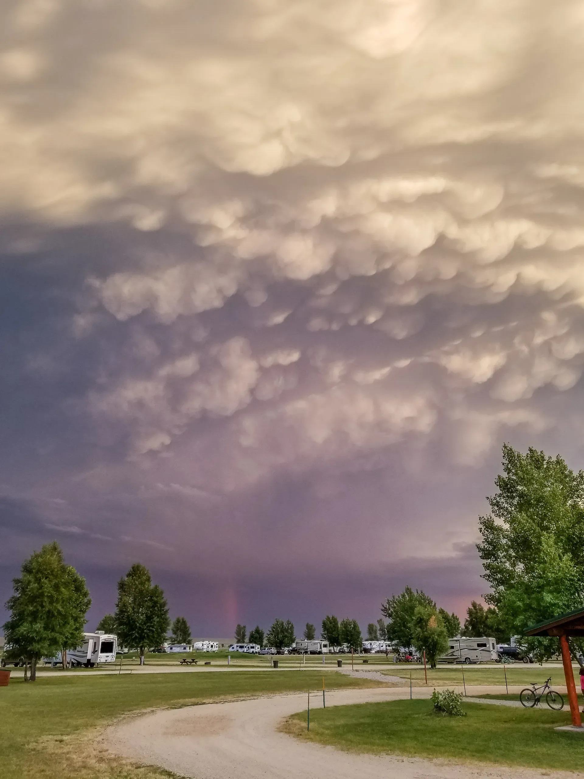 Overcast sky with mammatus clouds over a campground with trees, RVs, and a winding path.