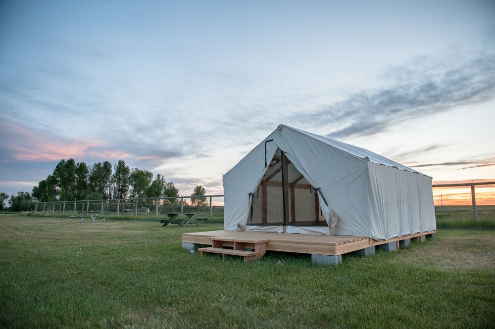 Canvas tent on a wooden platform in a grassy field under a twilight sky.