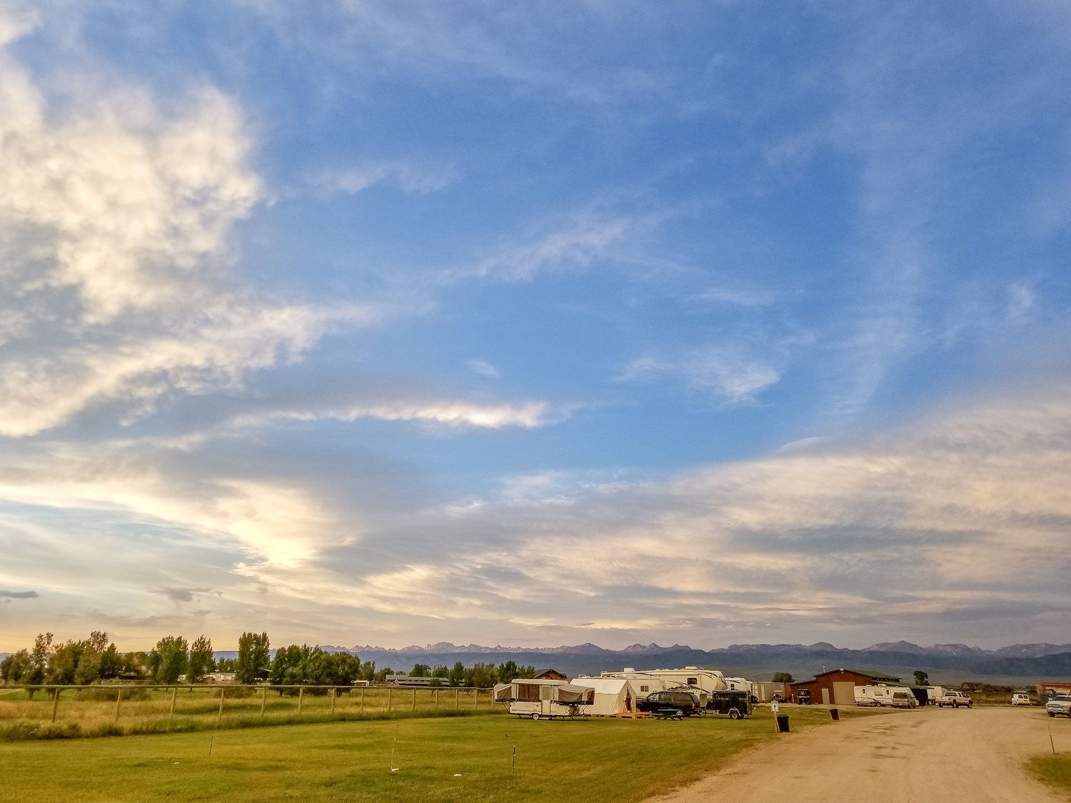 Blue sky with clouds over a grassy field, RVs, and mountains.