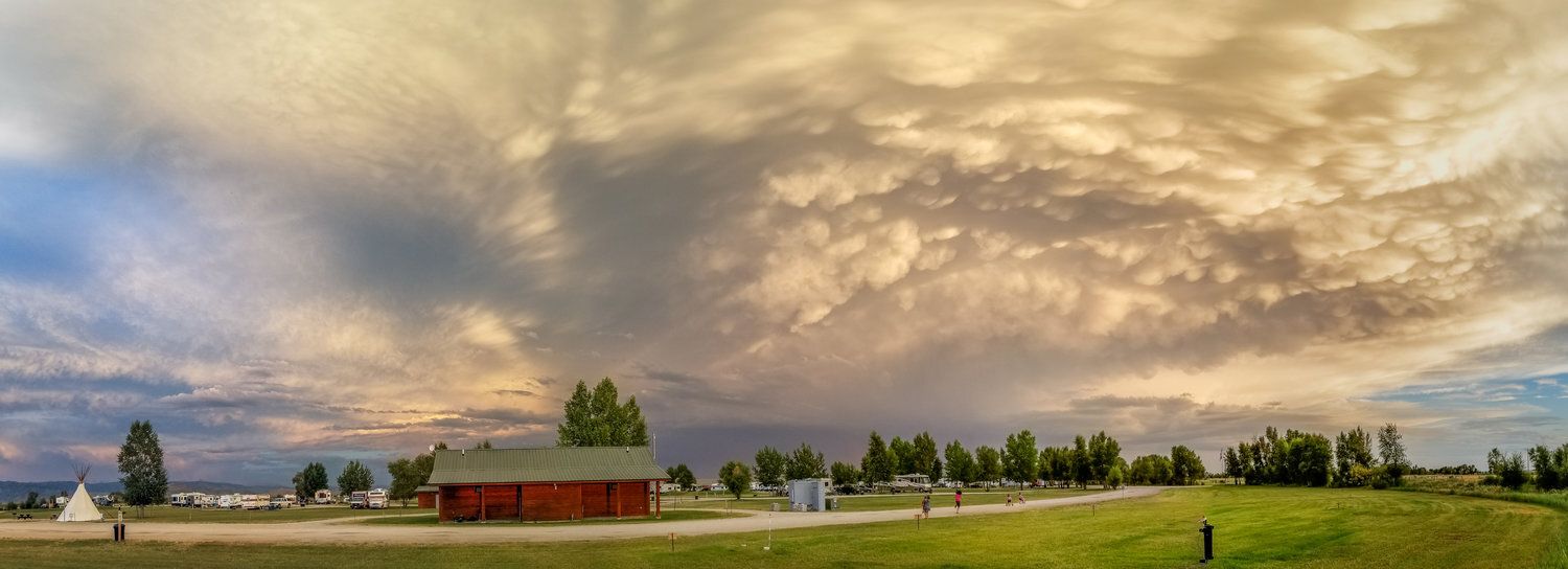 Dramatic, panoramic sky over a rural landscape, red building, trees, and grass.