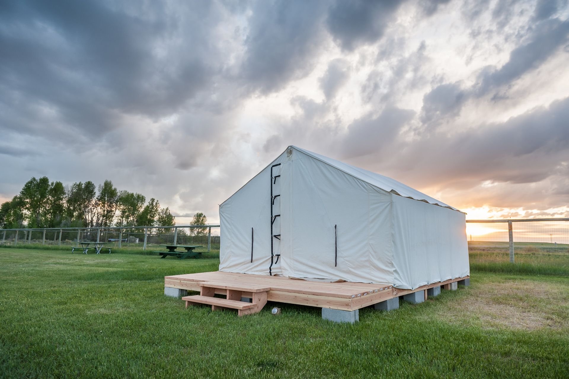 White canvas tent on a wooden platform in a grassy field with a cloudy sky.