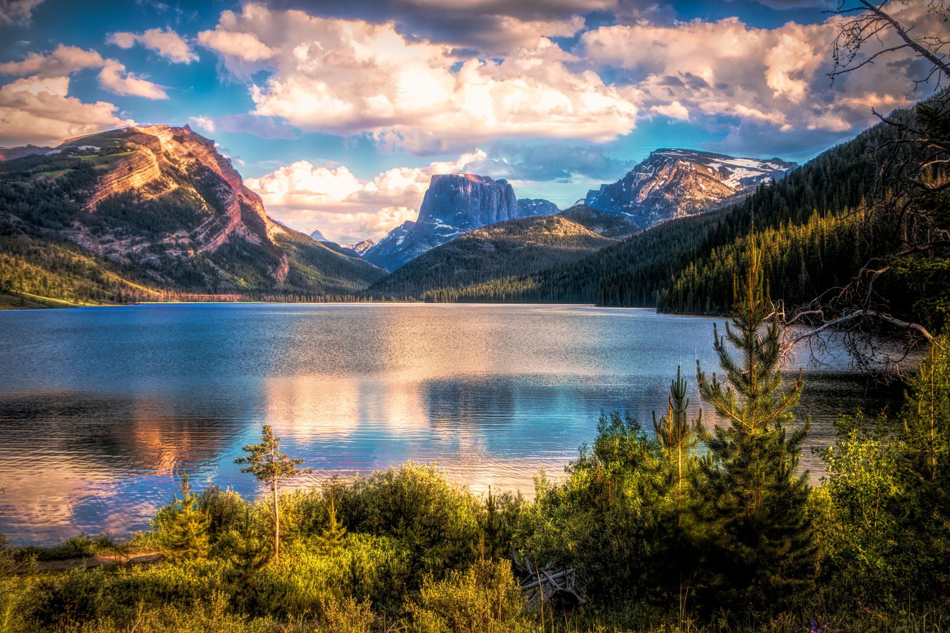 Lake surrounded by mountains and lush greenery under a cloudy sky, reflecting in the water.