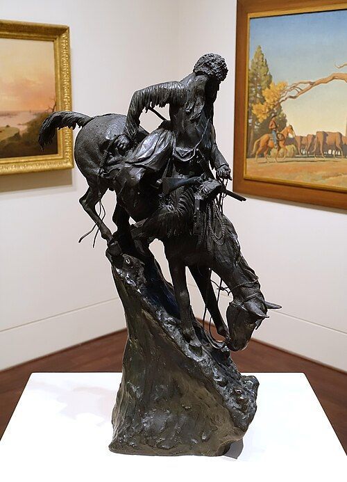 Bronze statue of a Native American man on horseback, horse drinking from a water source.