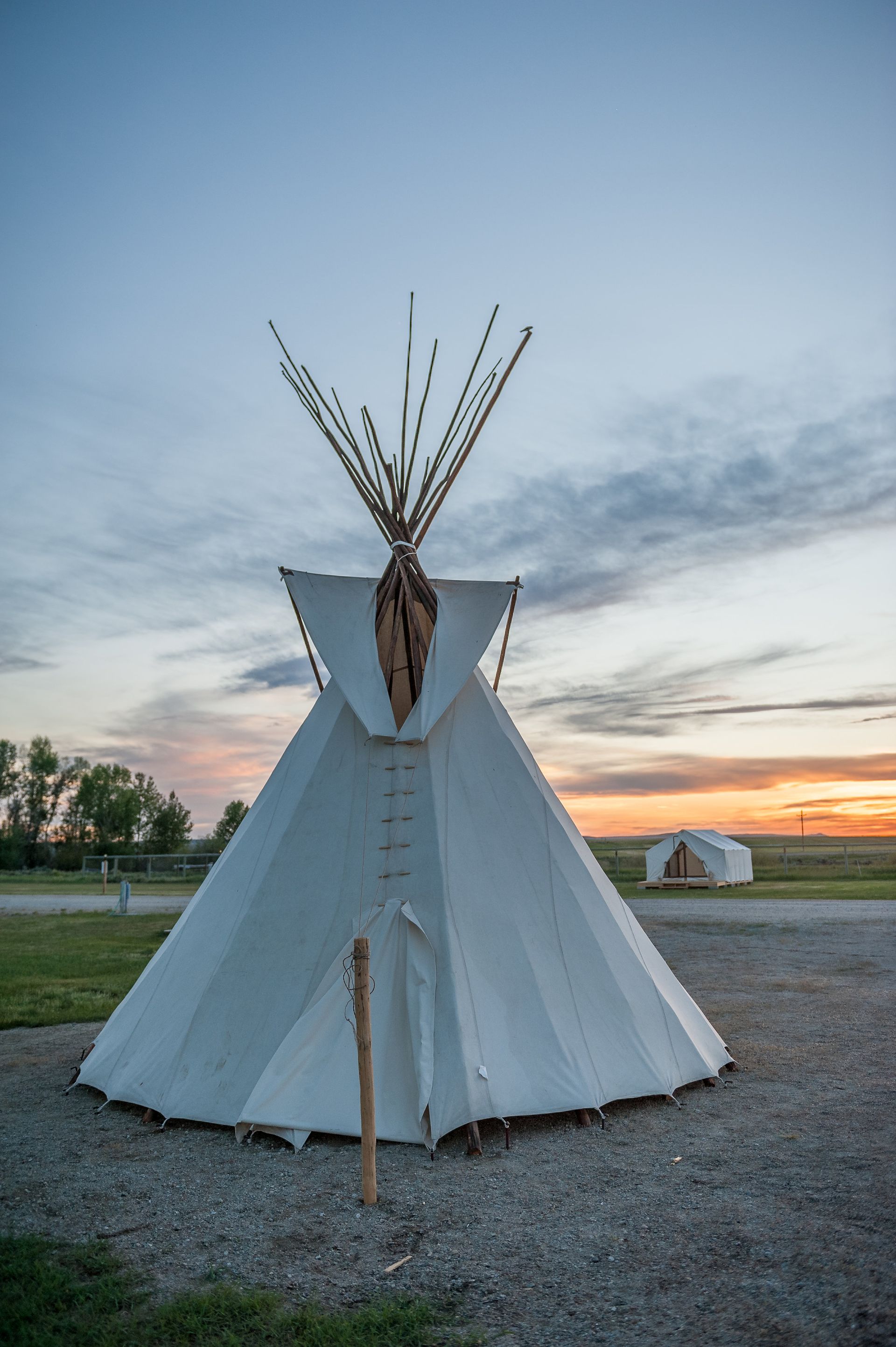 White teepee against a colorful sunset sky; another tent visible in the distance.