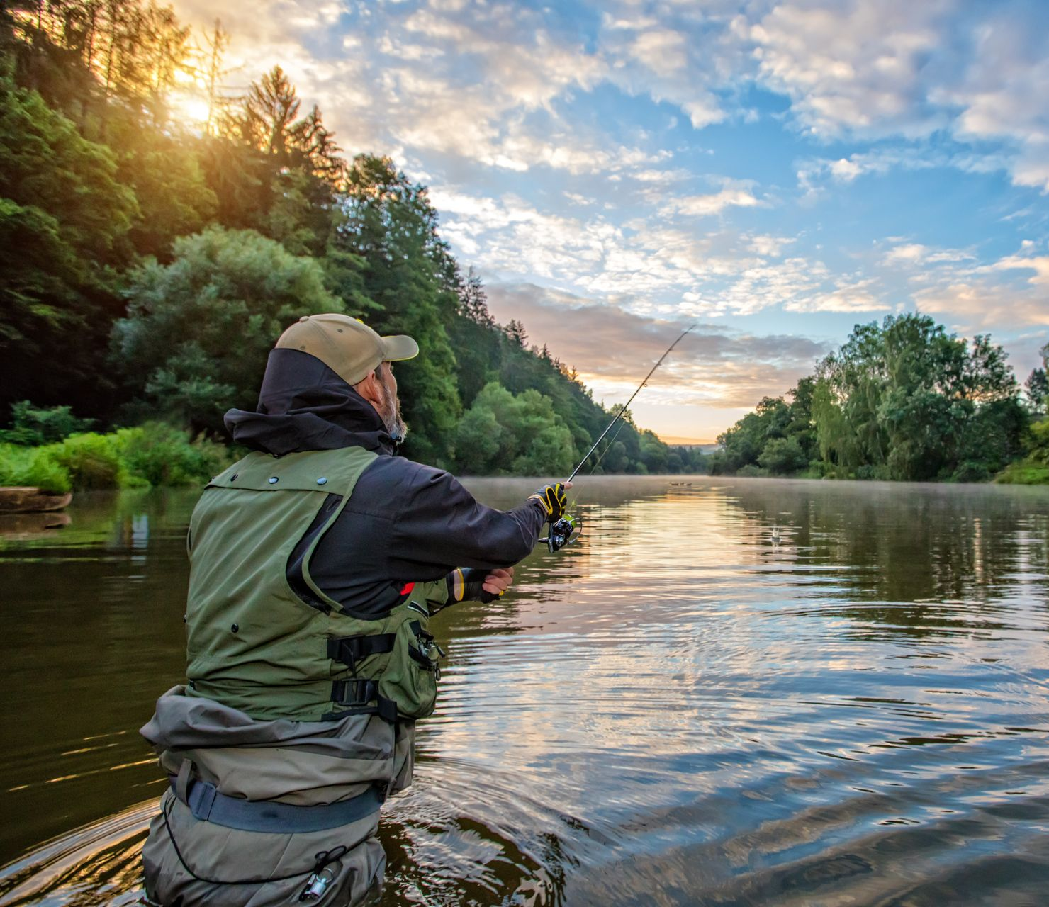 Person fishing in a river, holding a rod, wearing a vest, surrounded by trees, with a sunrise.