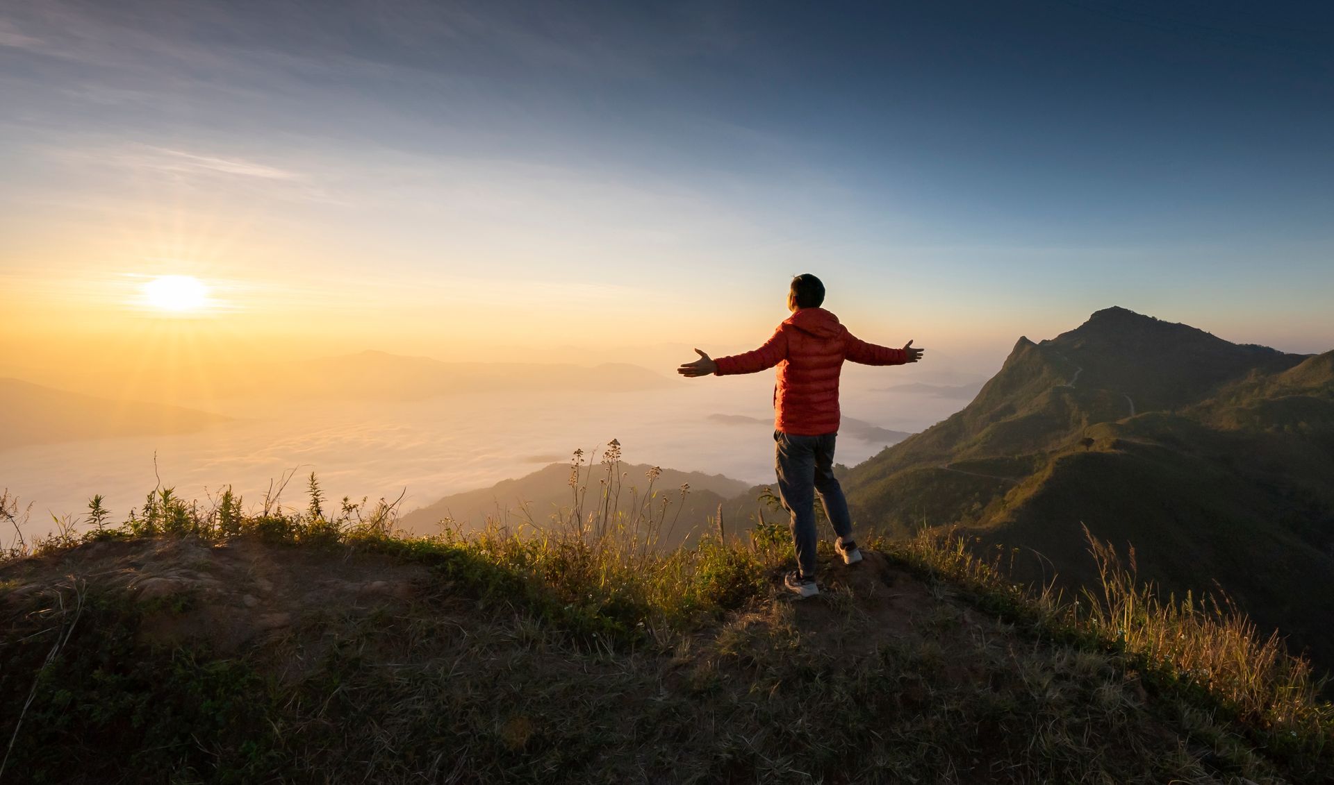Person with arms outstretched on mountain ridge at sunrise.