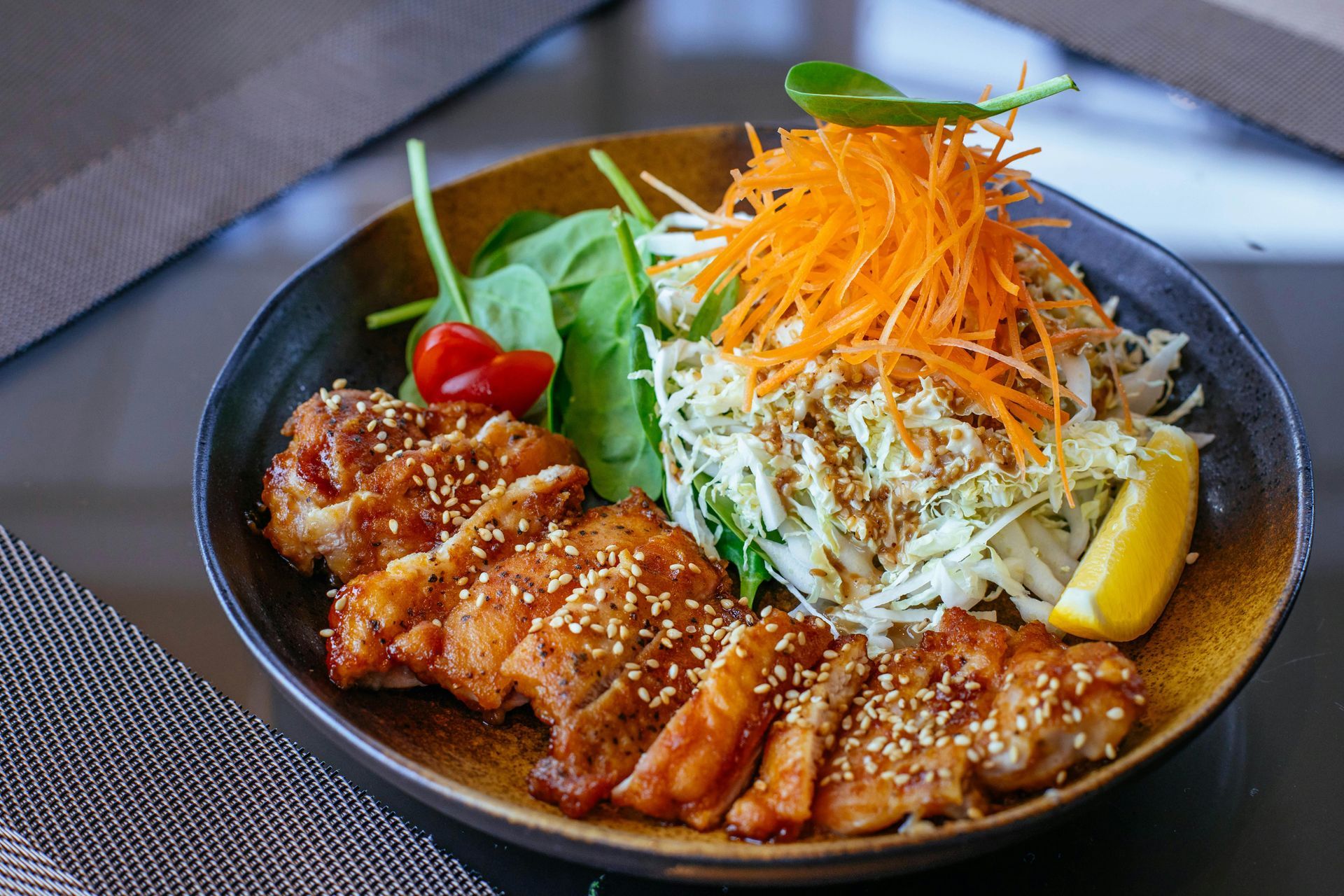 Teriyaki chicken dish with shredded vegetables and lemon wedge.