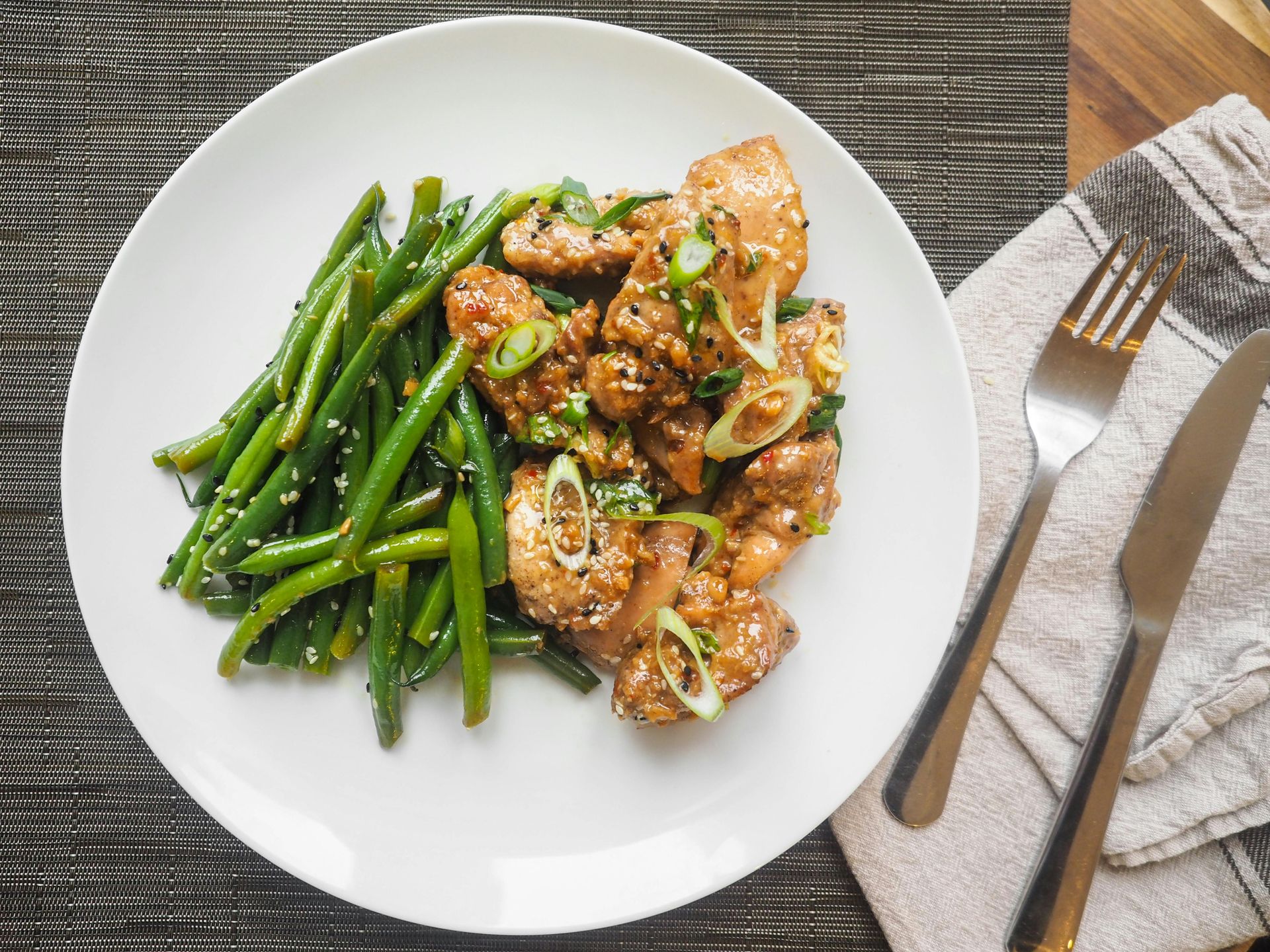 Chicken stir-fry with green beans and sesame seeds on a white plate, served with a fork and knife.