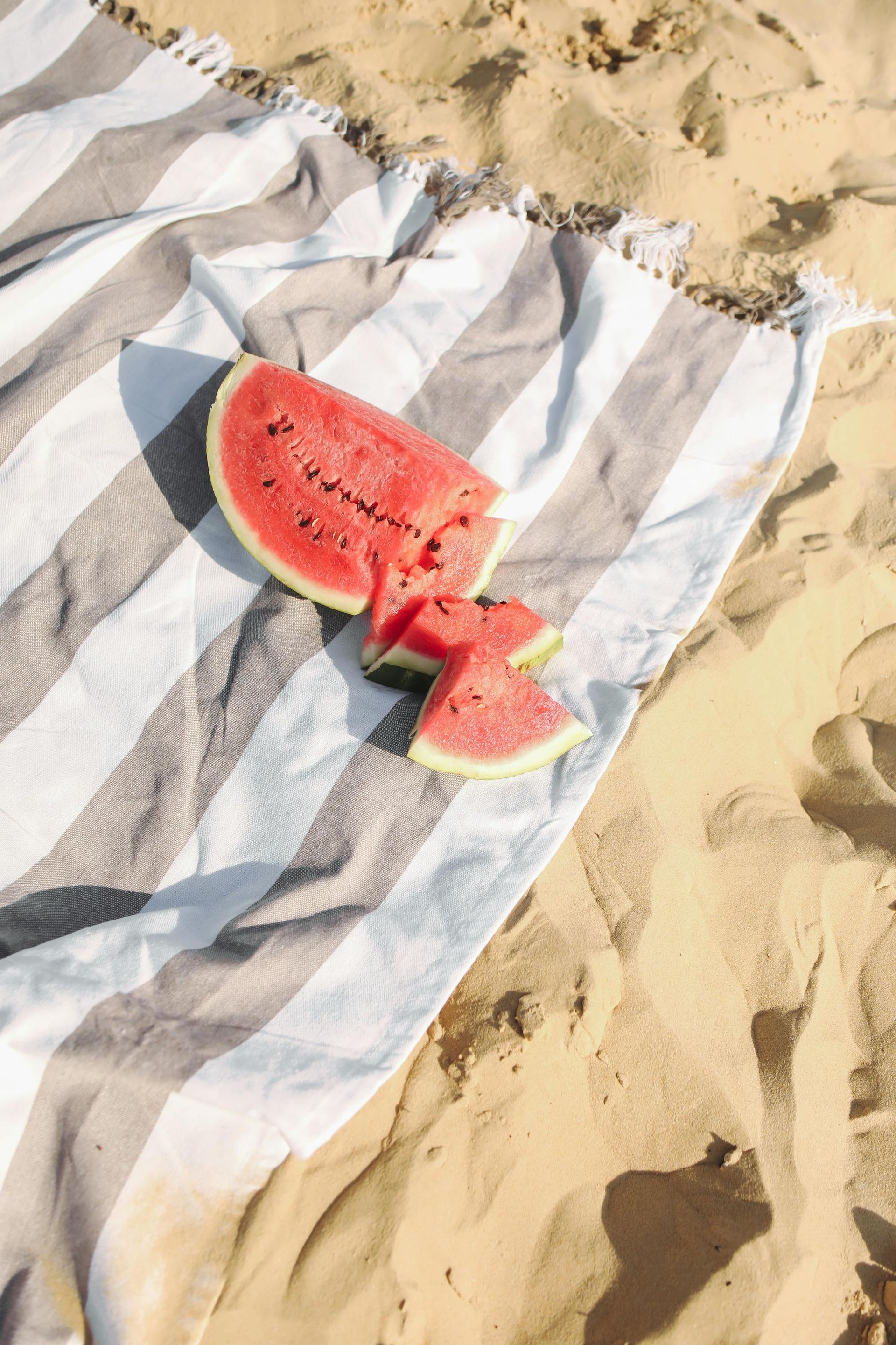 Watermelon slices on striped towel at beach.