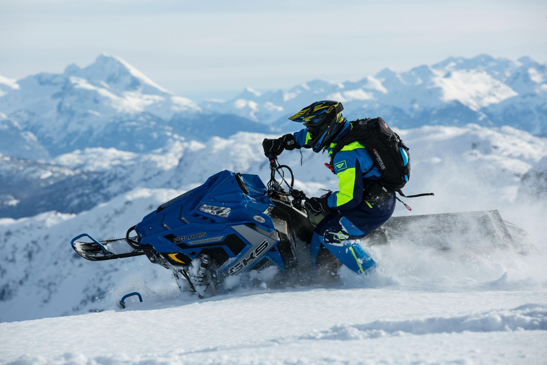 Snowmobiler riding a blue snowmobile in snowy mountains.